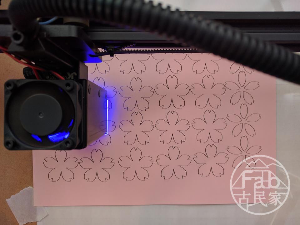 レーザー加工機でピンク色の色紙を桜の形にカット